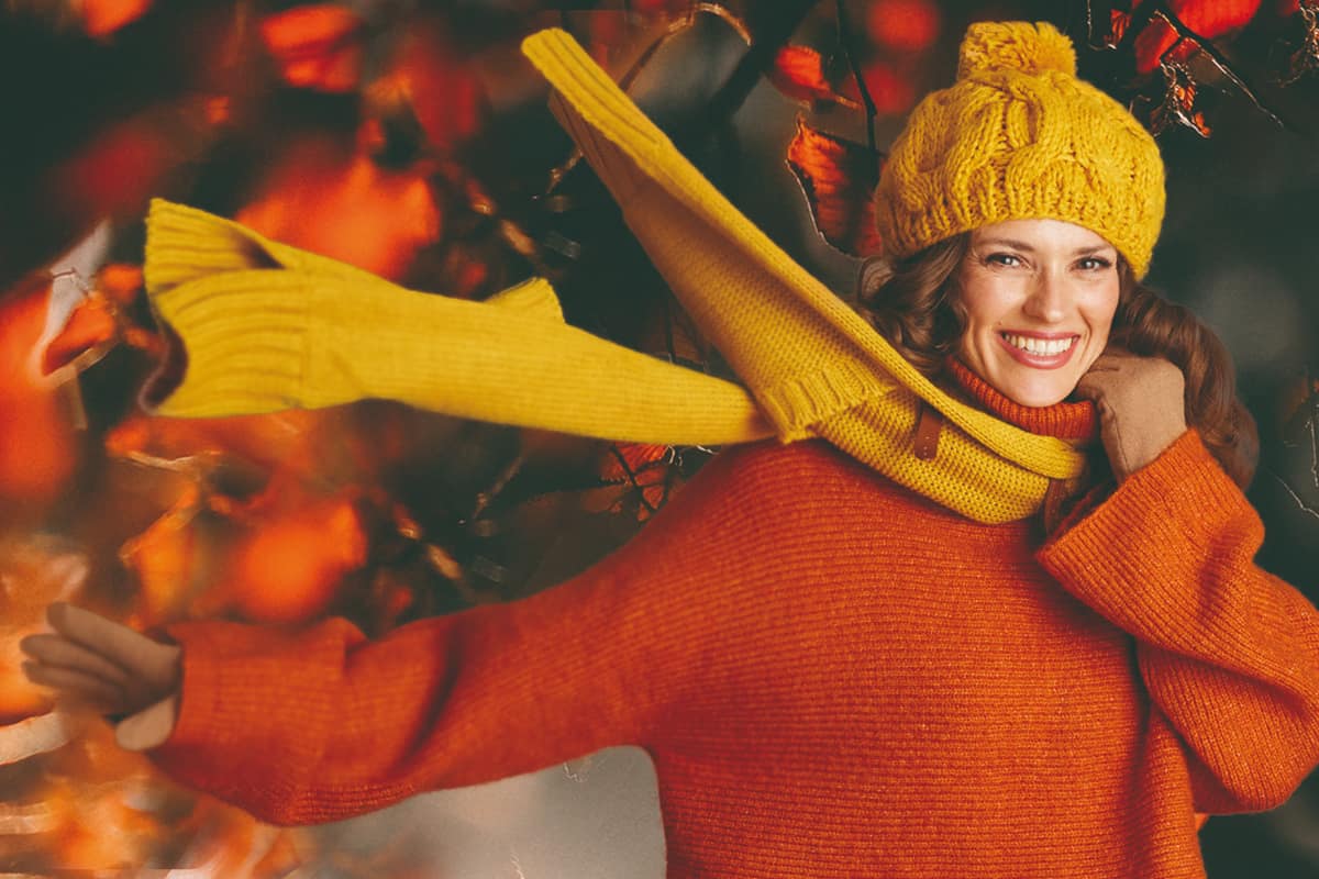 Frau mit Mütze und Schal, die lacht vor herbstlichem Hintergrund.